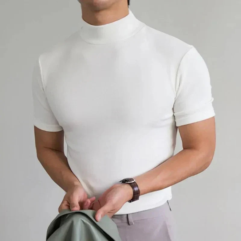Uomo in maglia bianca a collo alto, maniche corte, tiene giacca verde. Moda maschile elegante, abbigliamento casual chic.
