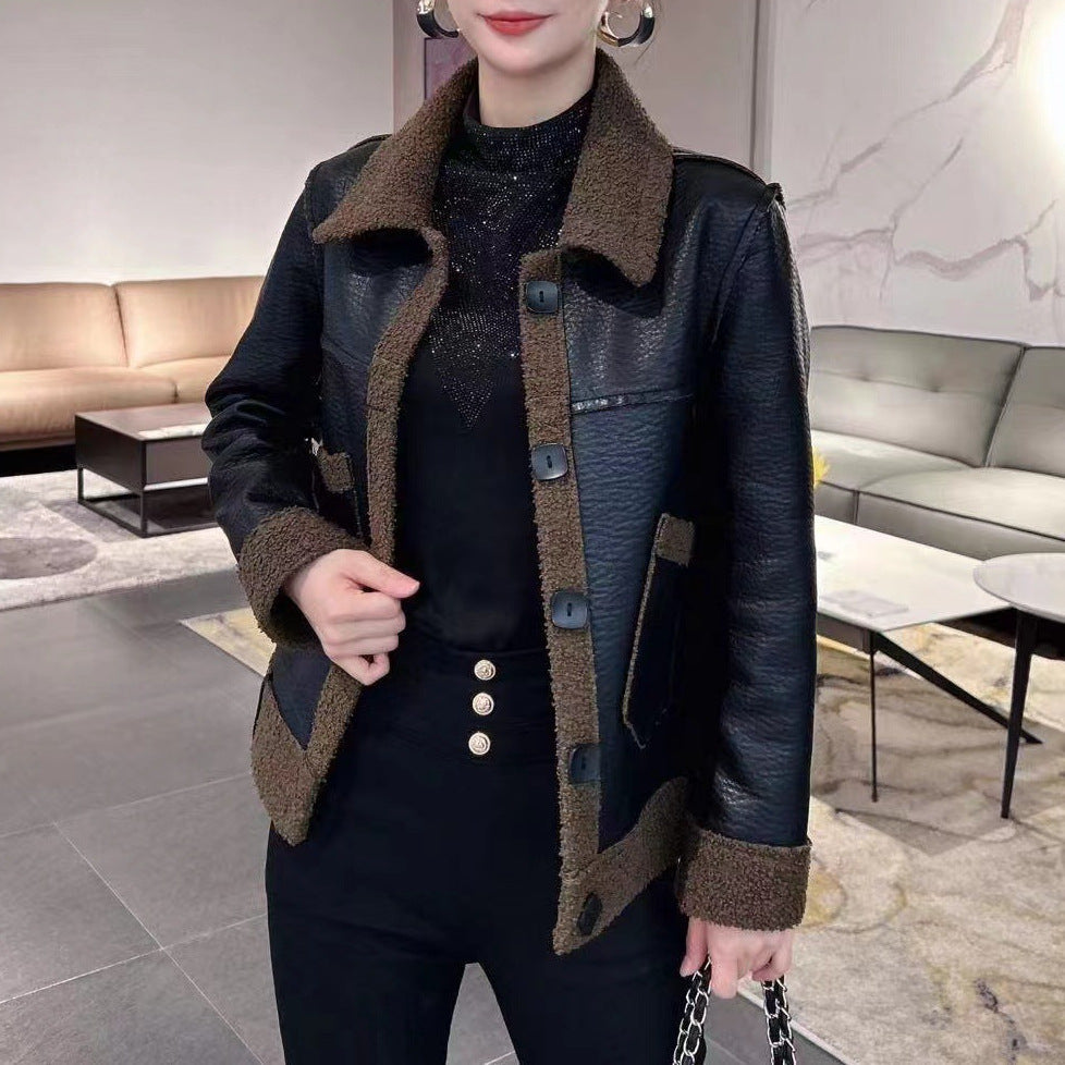 Donna con giacca in pelle nera e dettagli marroni, maglia nera scintillante, pantaloni neri con bottoni dorati, in un salotto moderno.