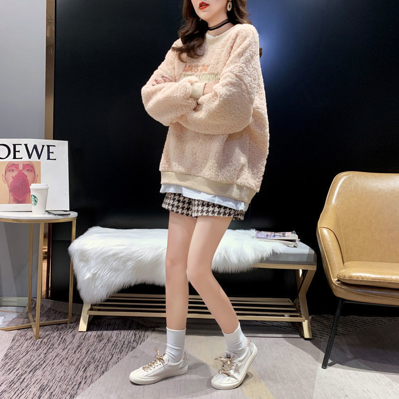 Donna con maglione oversize beige, gonna a quadri e sneakers bianche. Look casual chic, moda autunnale, stile urbano.