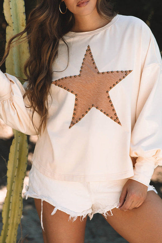 Donna con maglia beige con stella decorata, pantaloncini bianchi, accanto a cactus. Moda casual, abbigliamento estivo, stile trendy.