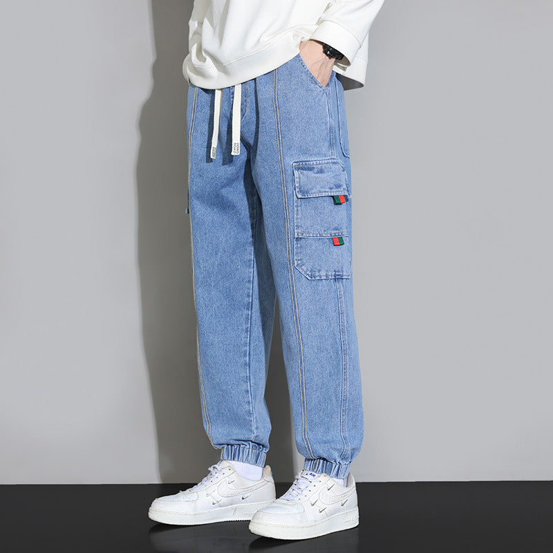 Pantaloni cargo in denim azzurro con tasche multiple, indossati con sneakers bianche. Stile casual, moda uomo, abbigliamento urbano.