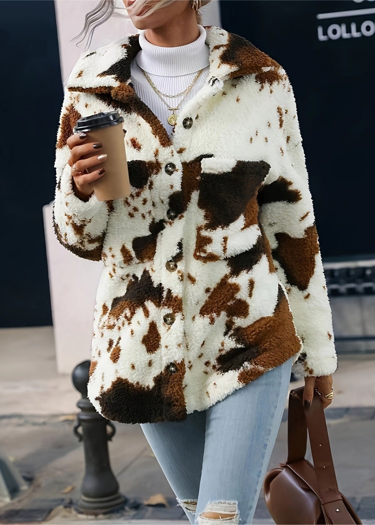 Donna con giacca in pelliccia sintetica maculata bianca e marrone, jeans strappati, maglione bianco, collane dorate, caffè da asporto, borsa marrone.