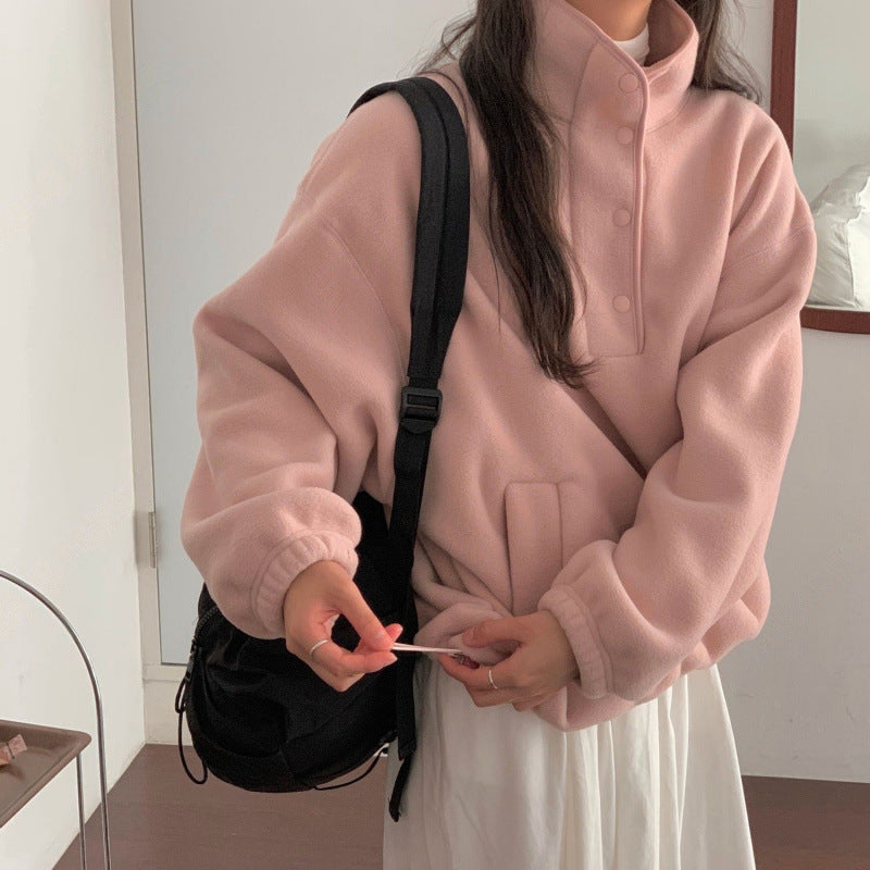 Donna con felpa rosa oversize e zaino nero, in piedi in una stanza minimalista. Moda casual autunnale, abbigliamento comodo e trendy.