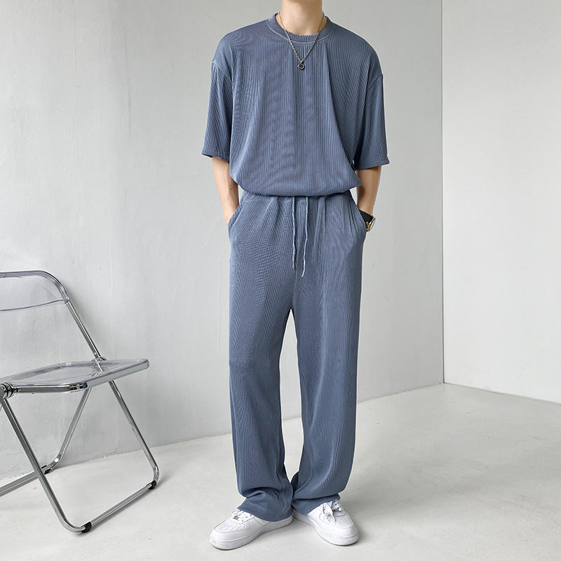 Uomo in tuta grigia casual, con maglietta e pantaloni coordinati, indossa scarpe bianche. Stile minimalista, moda uomo contemporanea.