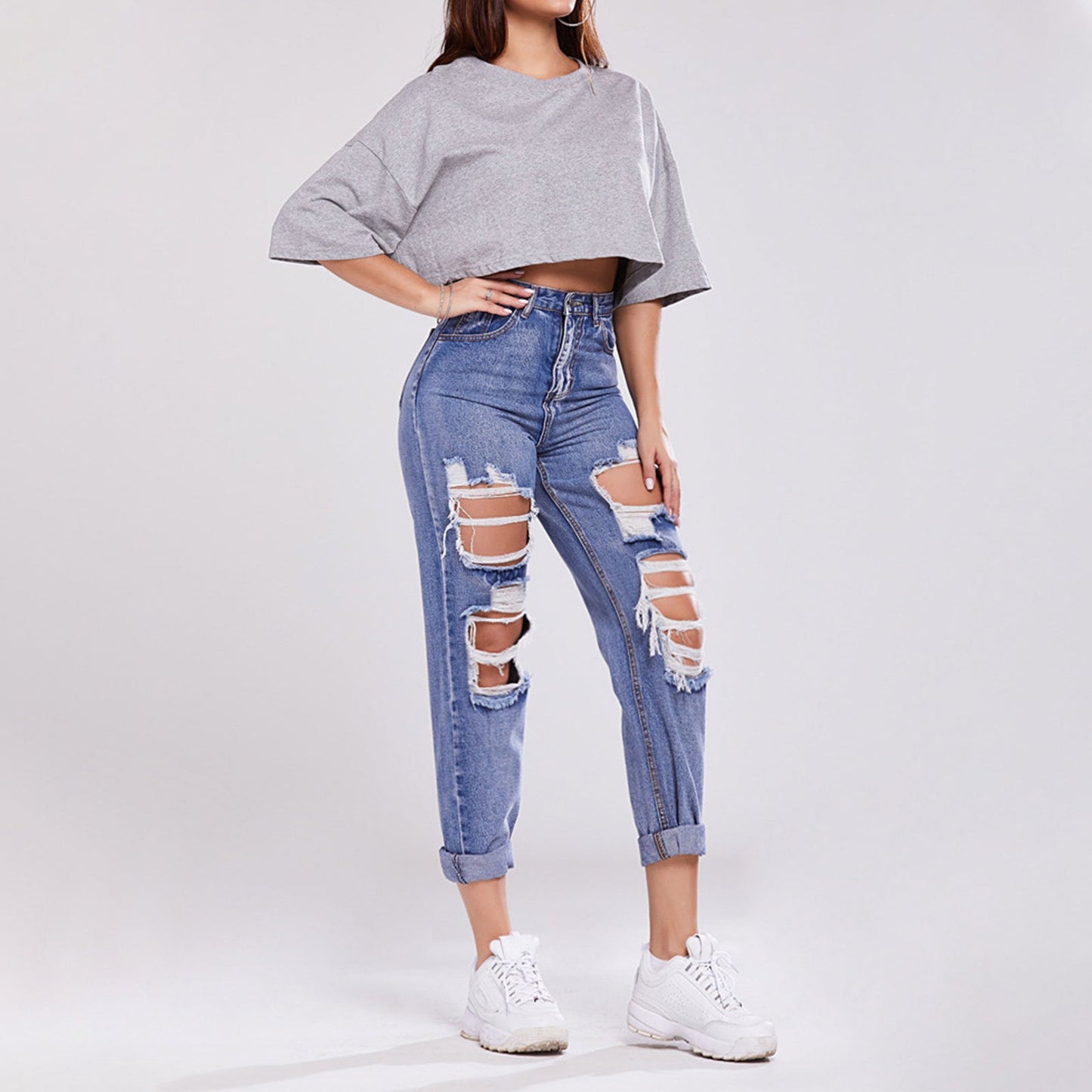 Donna in jeans strappati e top grigio, scarpe da ginnastica bianche. Moda casual, abbigliamento trendy, stile urbano.