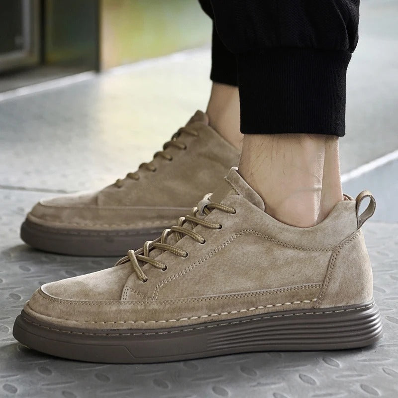 Scarpe da ginnastica beige in pelle scamosciata, suola marrone, indossate da una persona su pavimento metallico. Moda casual, calzature uomo eleganti.