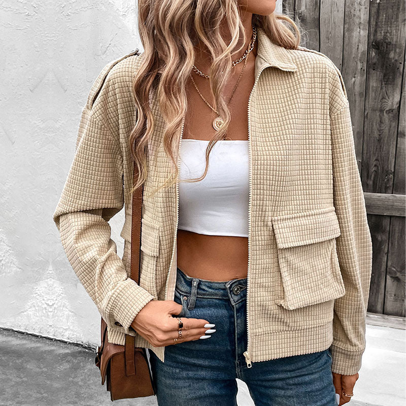 Donna con giacca beige a quadri, top bianco e jeans, indossa collana dorata. Moda casual autunnale, stile urbano, outfit trendy.