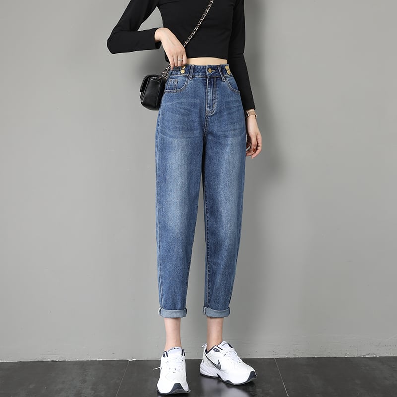 Donna in jeans a vita alta e sneakers bianche, indossa una maglia nera a maniche lunghe e borsa a tracolla. Moda casual femminile.