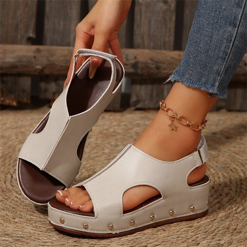 Sandali estivi bianchi con zeppa e borchie, indossati con jeans. Design aperto, cinturino alla caviglia, perfetti per look casual e alla moda.