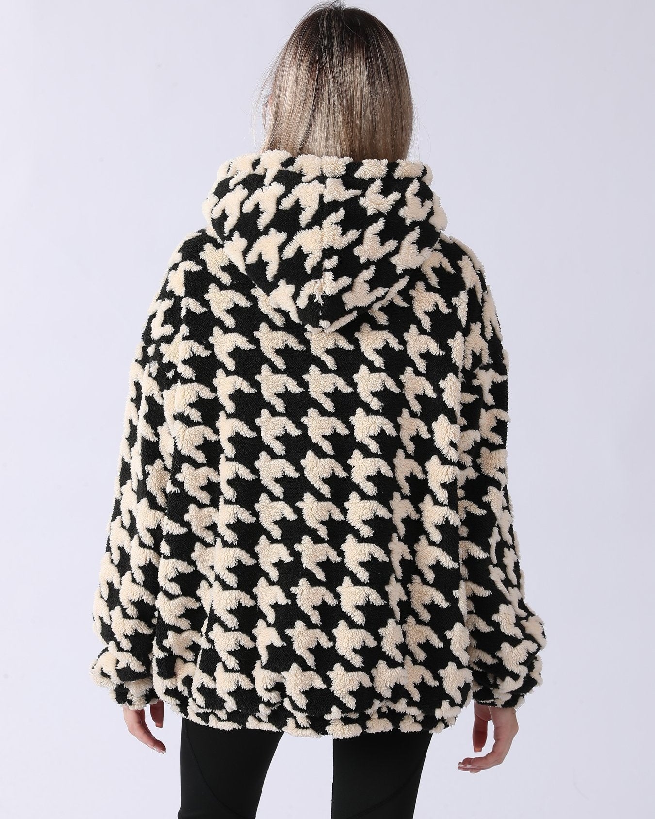 Donna con cappotto in pile a fantasia pied de poule bianco e nero, vista posteriore. Moda invernale, abbigliamento caldo e accogliente.