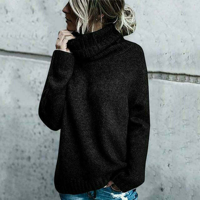 Donna con maglione nero a collo alto, capelli raccolti, posa contro muro grigio. Moda autunno inverno, abbigliamento casual elegante.