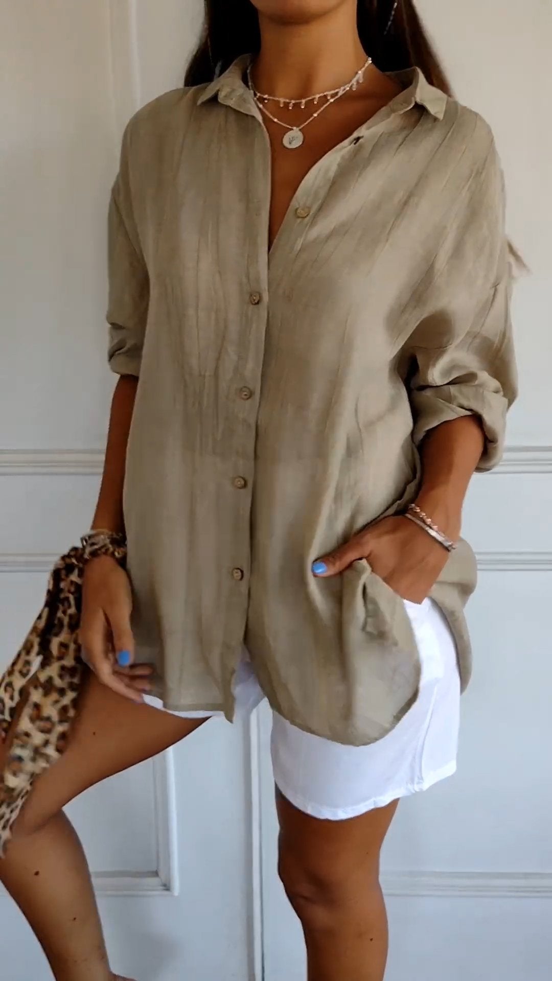 Camicia beige oversize in lino, abbinata a pantaloncini bianchi. Look estivo casual con accessori leopardati e collane a strati.