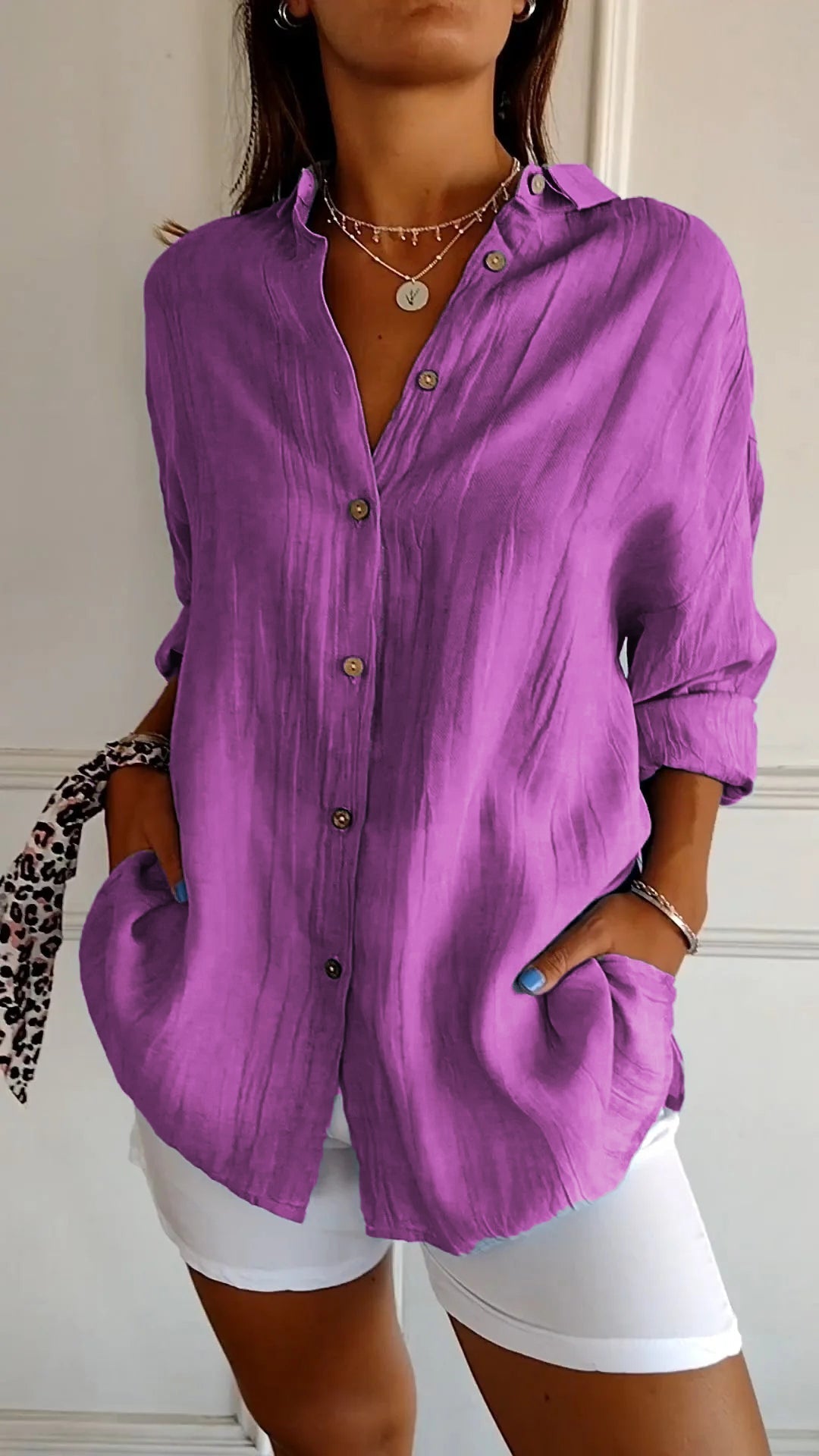 Camicia viola da donna in lino con bottoni, maniche lunghe e tasche, abbinata a pantaloni bianchi. Stile casual elegante, moda femminile.