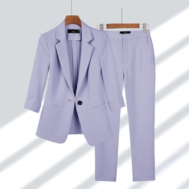 Completo donna elegante color lavanda, giacca e pantaloni abbinati, appesi su grucce di legno. Moda femminile, abbigliamento formale.