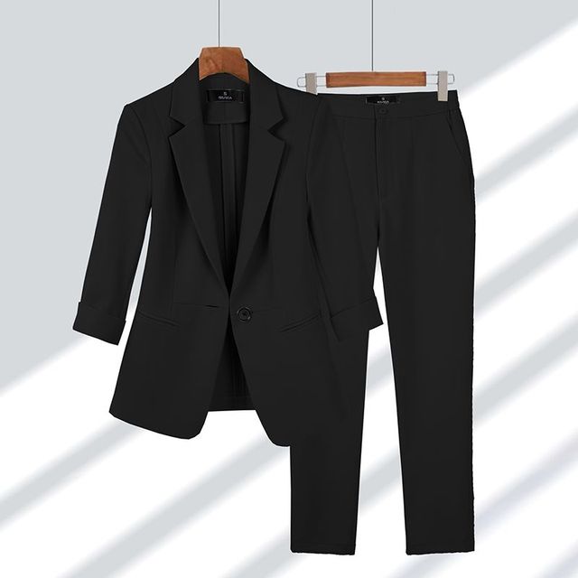 Completo elegante nero da donna, giacca e pantaloni abbinati, appesi su grucce di legno. Moda formale, abbigliamento da ufficio.