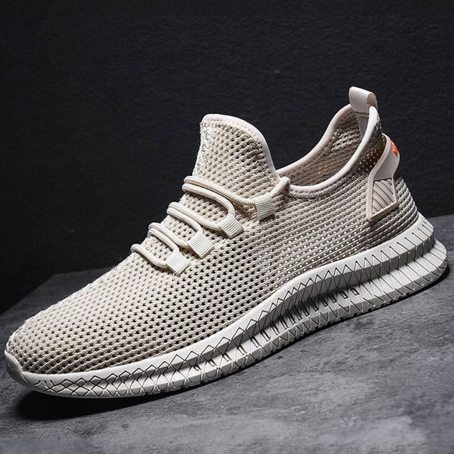 Scarpa da ginnastica beige in maglia traspirante su sfondo grigio, design moderno, suola antiscivolo, ideale per sport e tempo libero.