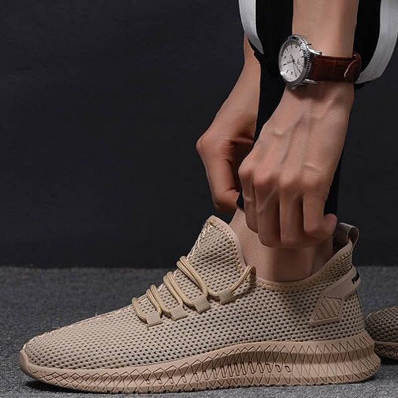 Scarpa sportiva beige con design a rete, suola antiscivolo e lacci, indossata da una persona con orologio al polso. Scarpe da ginnastica moderne.