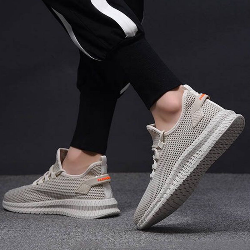 Scarpe da ginnastica beige in maglia traspirante, suola antiscivolo, indossate da una persona in pantaloni sportivi neri.