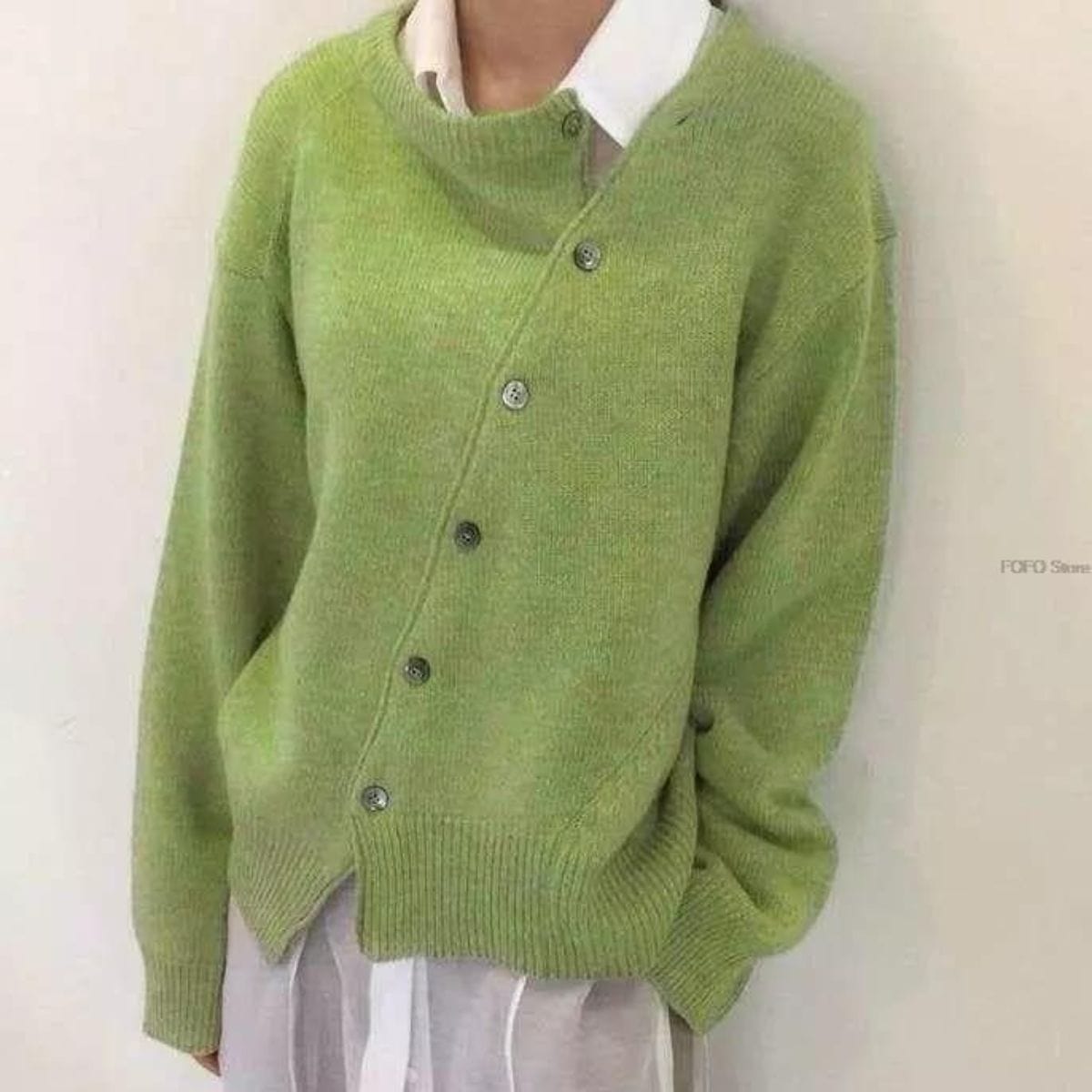 Cardigan verde asimmetrico con bottoni, indossato sopra una camicia bianca. Moda autunnale, abbigliamento casual elegante, tendenze 2023.