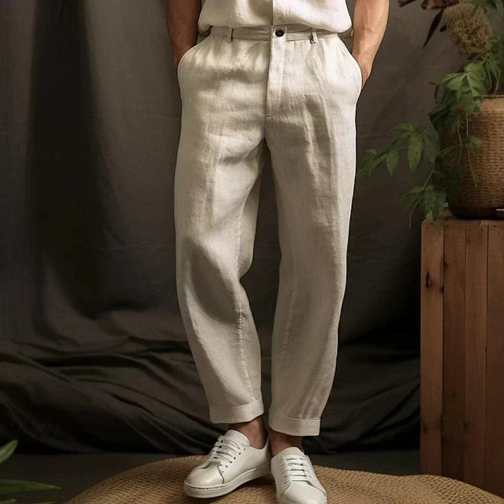 Pantaloni di lino beige eleganti, abbinati a scarpe bianche, su sfondo naturale con piante. Moda uomo, stile casual chic.