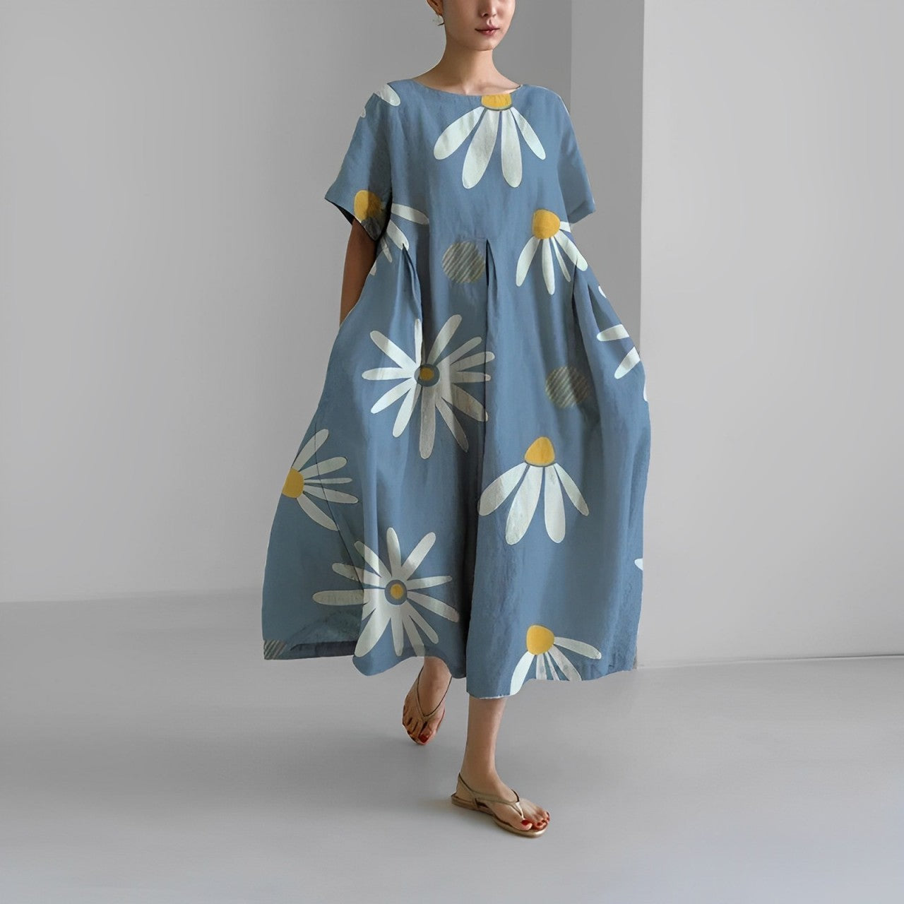 Abito lungo estivo blu con stampa floreale margherite bianche e gialle, maniche corte, indossato da donna con sandali beige. Moda casual elegante.