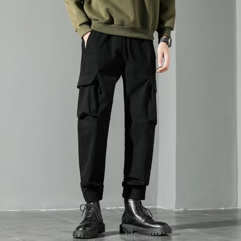 Pantaloni cargo neri da uomo, stile casual, con tasche laterali, abbinati a stivali neri e felpa verde. Moda urbana, abbigliamento maschile trendy.