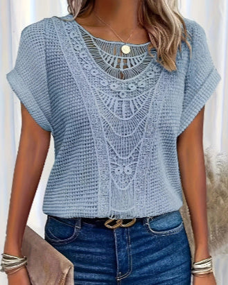 Donna con maglia azzurra lavorata a maglia, dettagli traforati, jeans blu, cintura nera e accessori dorati. Moda casual elegante.