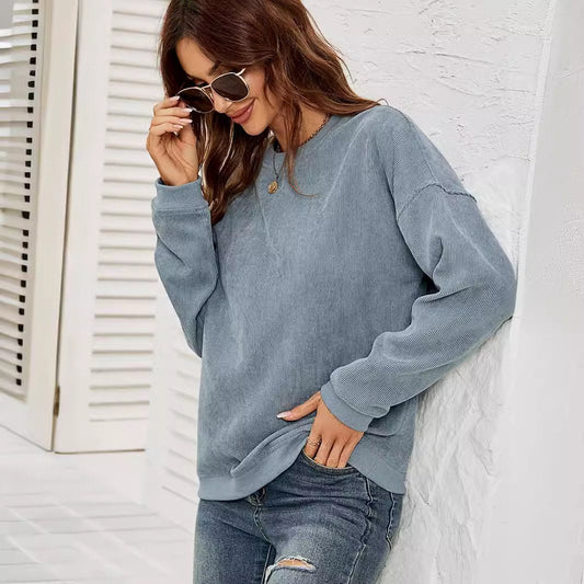 Donna con occhiali da sole indossa maglione blu casual e jeans, appoggiata a parete bianca. Moda autunnale, stile casual chic, abbigliamento femminile.