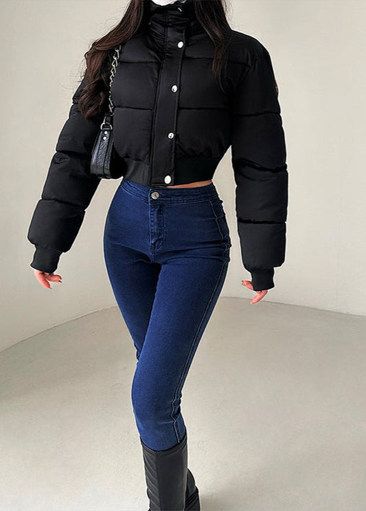 Donna in giacca nera imbottita e jeans aderenti blu, borsa a tracolla, posa in studio. Moda invernale, abbigliamento casual chic.