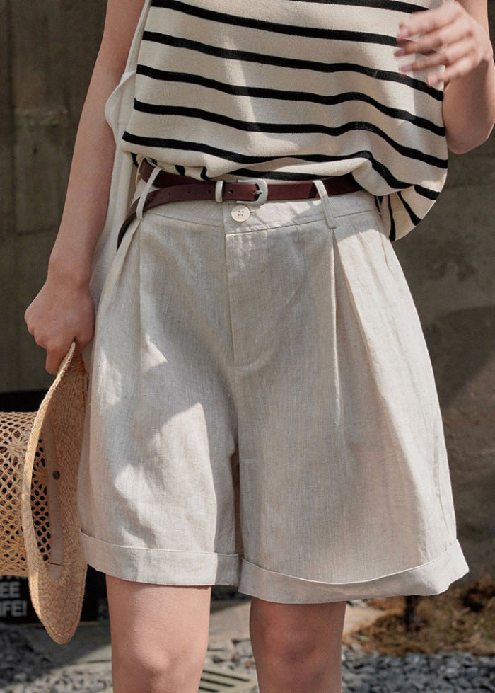 Donna con pantaloncini beige e cintura marrone, indossa maglia a righe bianche e nere, tiene cappello di paglia. Moda estiva casual.