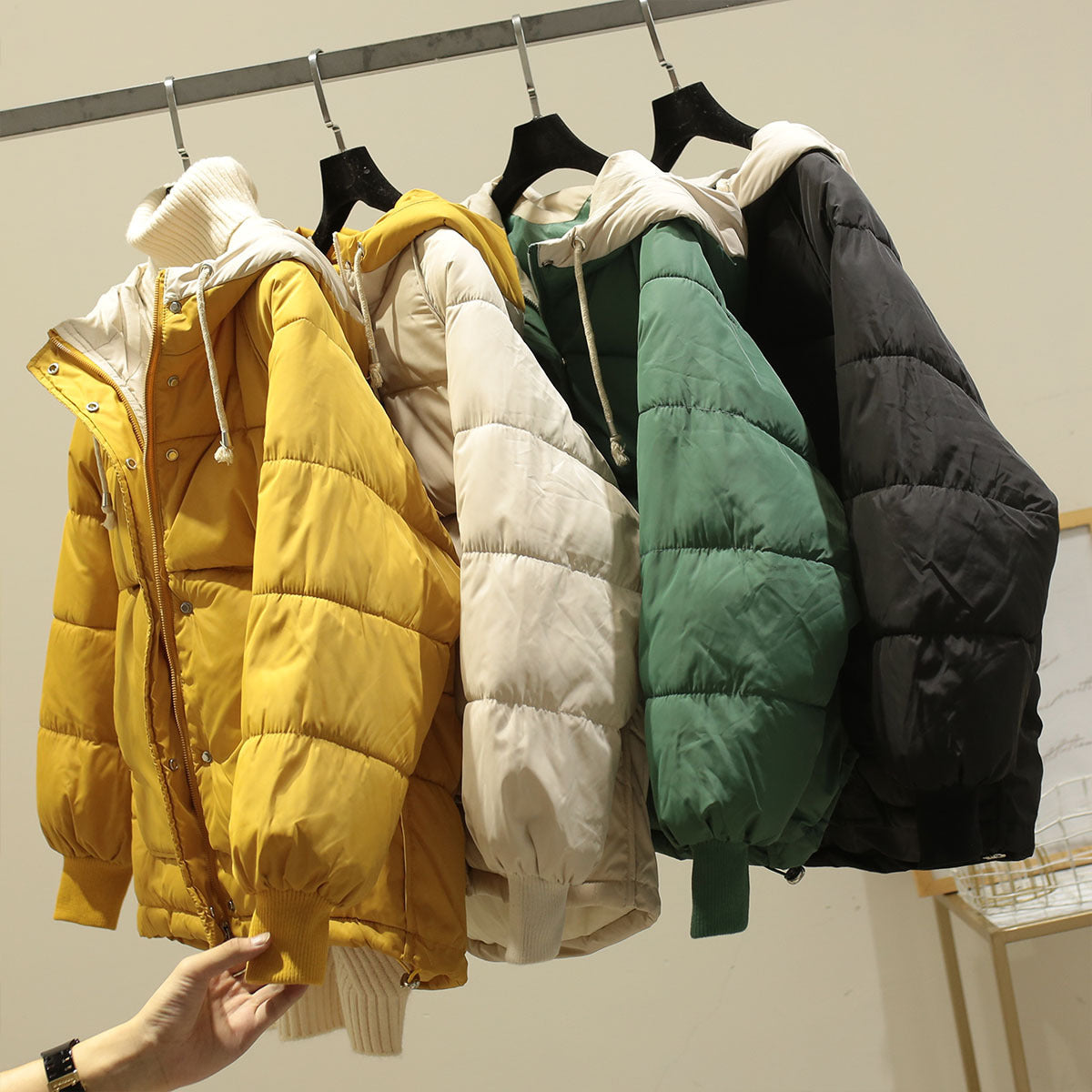 Giubbotti invernali imbottiti appesi: giallo, bianco, verde, nero. Moda calda, cappotti casual, abbigliamento invernale, tendenze 2023.