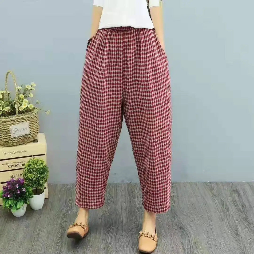 Pantaloni larghi a quadri rossi e bianchi, stile casual, indossati da una persona. Sfondo con piante decorative e pavimento in legno grigio.