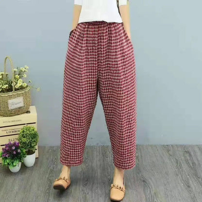 Pantaloni larghi a quadri rossi e bianchi, stile casual, indossati da una persona. Sfondo con piante decorative e pavimento in legno grigio.