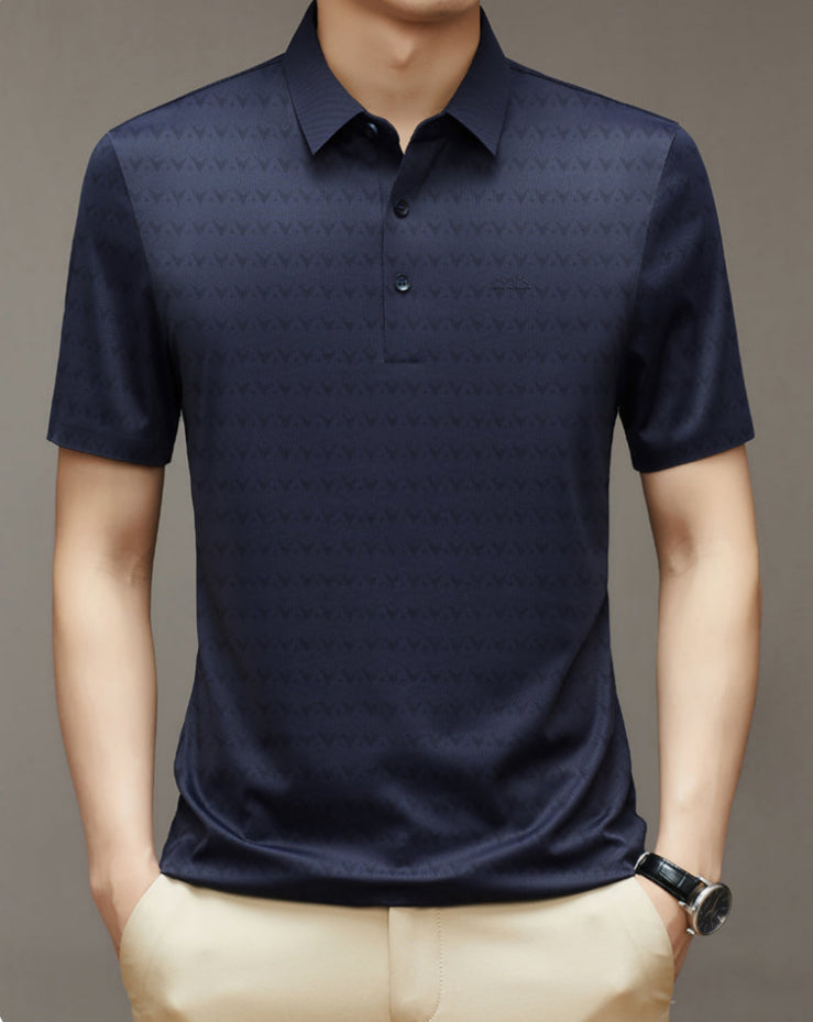 Uomo con polo blu scuro a maniche corte, motivo geometrico, indossa pantaloni beige e orologio nero. Moda maschile elegante e casual.