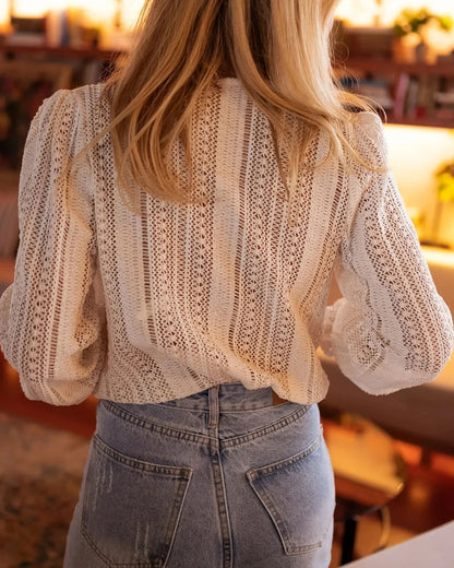 Donna di spalle con camicetta in pizzo bianco e jeans a vita alta, in un ambiente interno accogliente. Moda femminile, stile casual elegante.