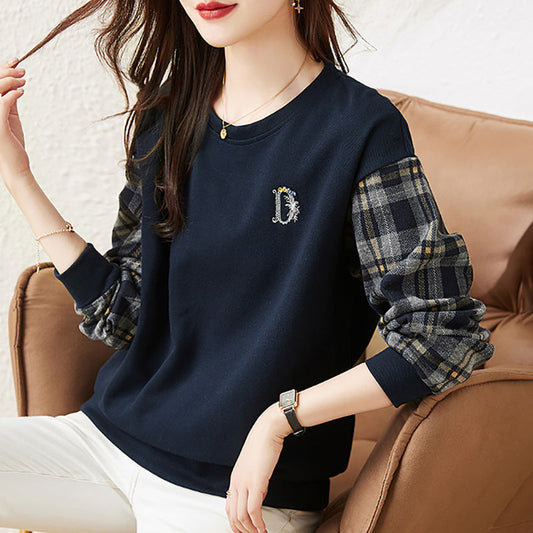 Donna seduta su poltrona indossa maglia blu con maniche a quadri, orologio e bracciale. Moda casual autunnale, abbigliamento femminile elegante.