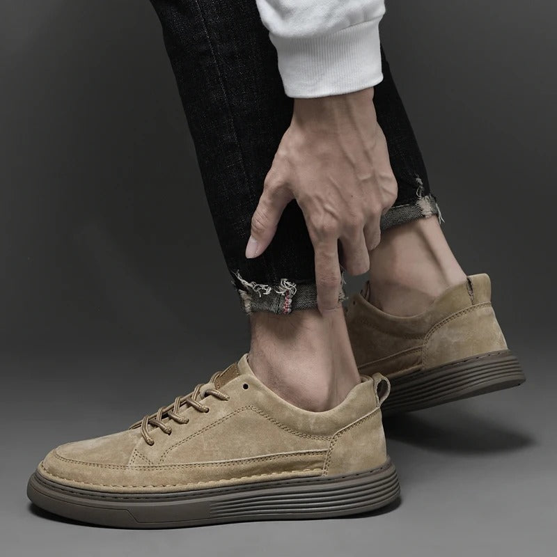 Scarpe da ginnastica beige in pelle scamosciata, indossate con jeans neri strappati. Design moderno, suola marrone, stile casual ed elegante.