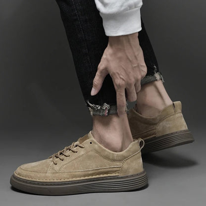 Scarpe da ginnastica beige in pelle scamosciata, indossate con jeans neri strappati. Design moderno, suola marrone, stile casual ed elegante.