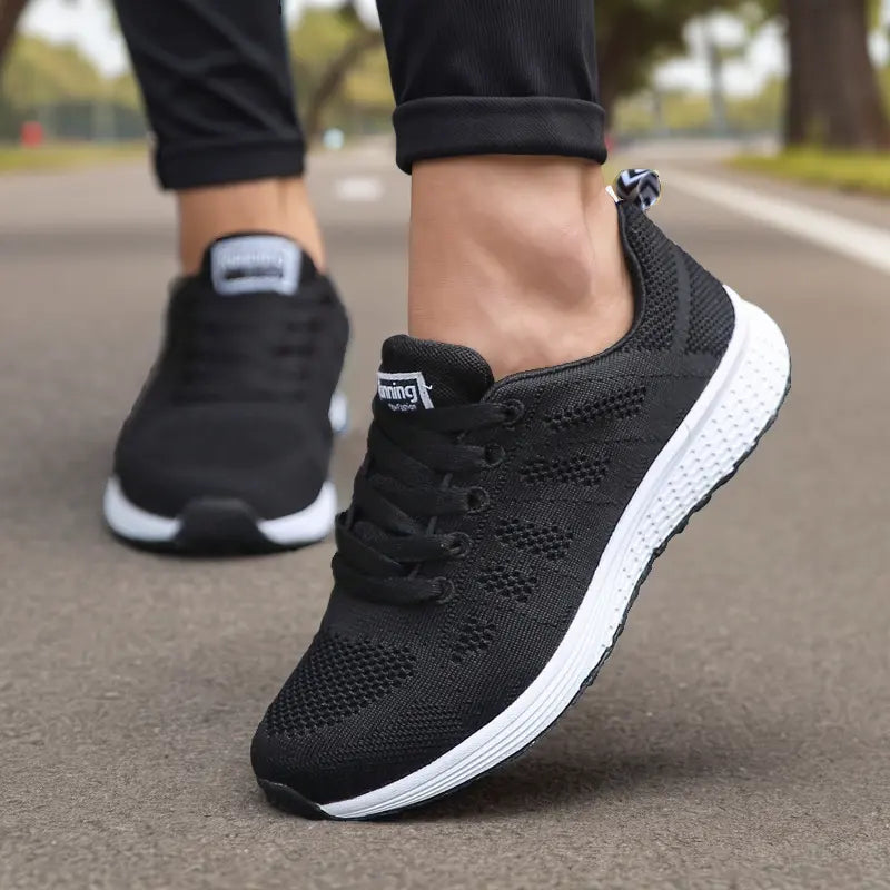 Scarpe da corsa nere su strada asfaltata, design traspirante, suola bianca ammortizzata, ideali per jogging e attività sportive all'aperto.
