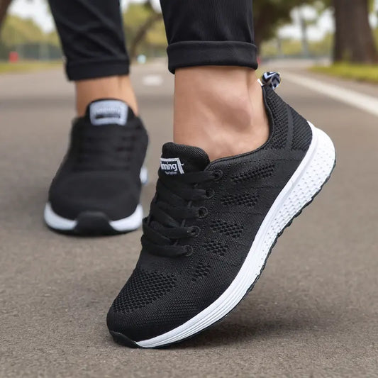 Scarpe da corsa nere su strada asfaltata, design traspirante, suola bianca ammortizzata, ideali per jogging e attività sportive all'aperto.