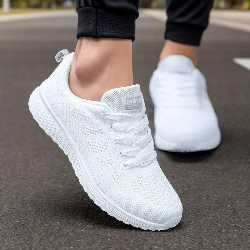 Scarpe da ginnastica bianche su strada asfaltata, design moderno e traspirante, perfette per corsa e sport. Scarpe sportive leggere e comode.