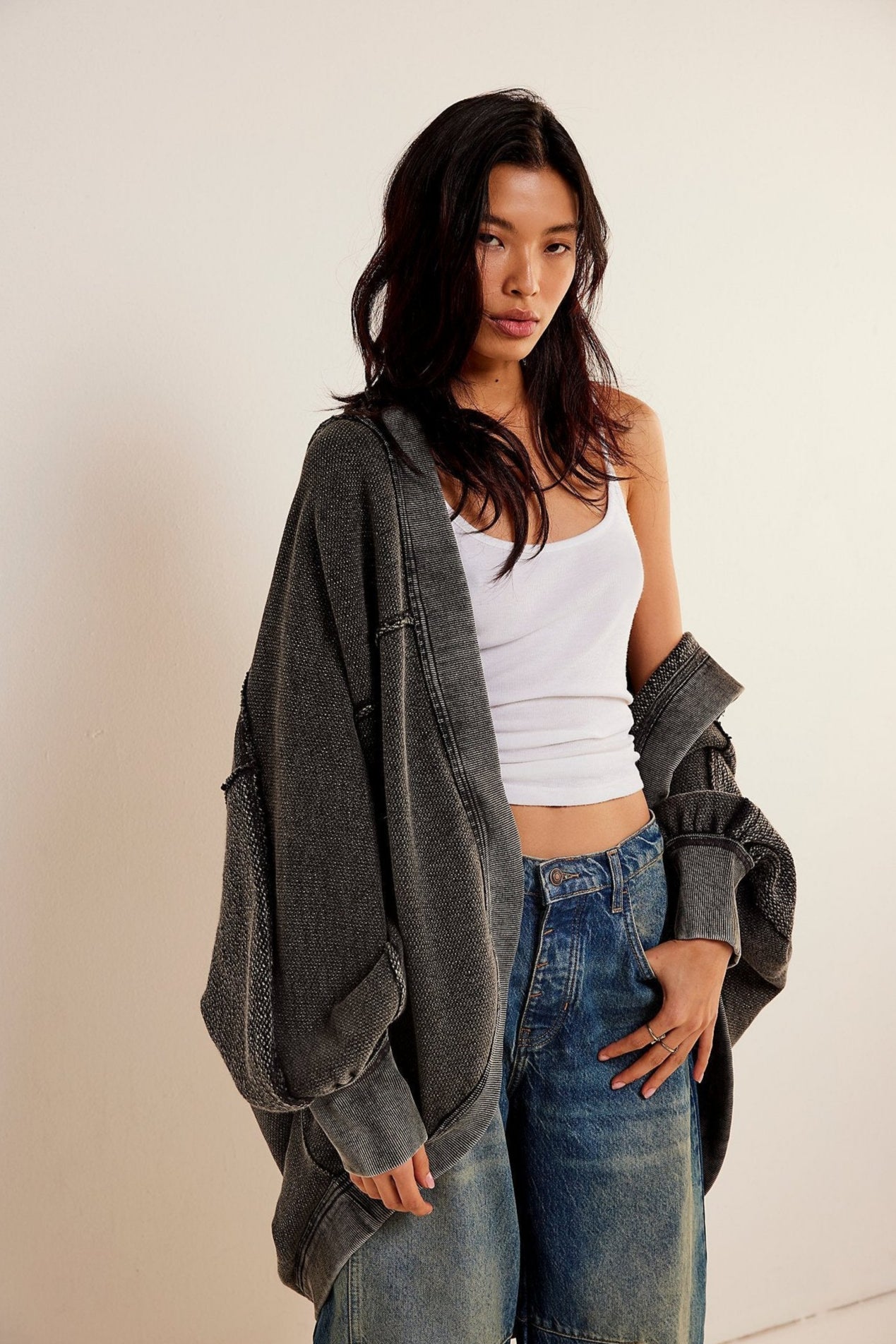 Donna con capelli scuri indossa canotta bianca, jeans larghi e giacca oversize grigia. Moda casual, stile urbano, abbigliamento trendy.