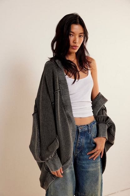 Donna con capelli scuri indossa canotta bianca, jeans larghi e giacca oversize grigia. Moda casual, stile urbano, abbigliamento trendy.