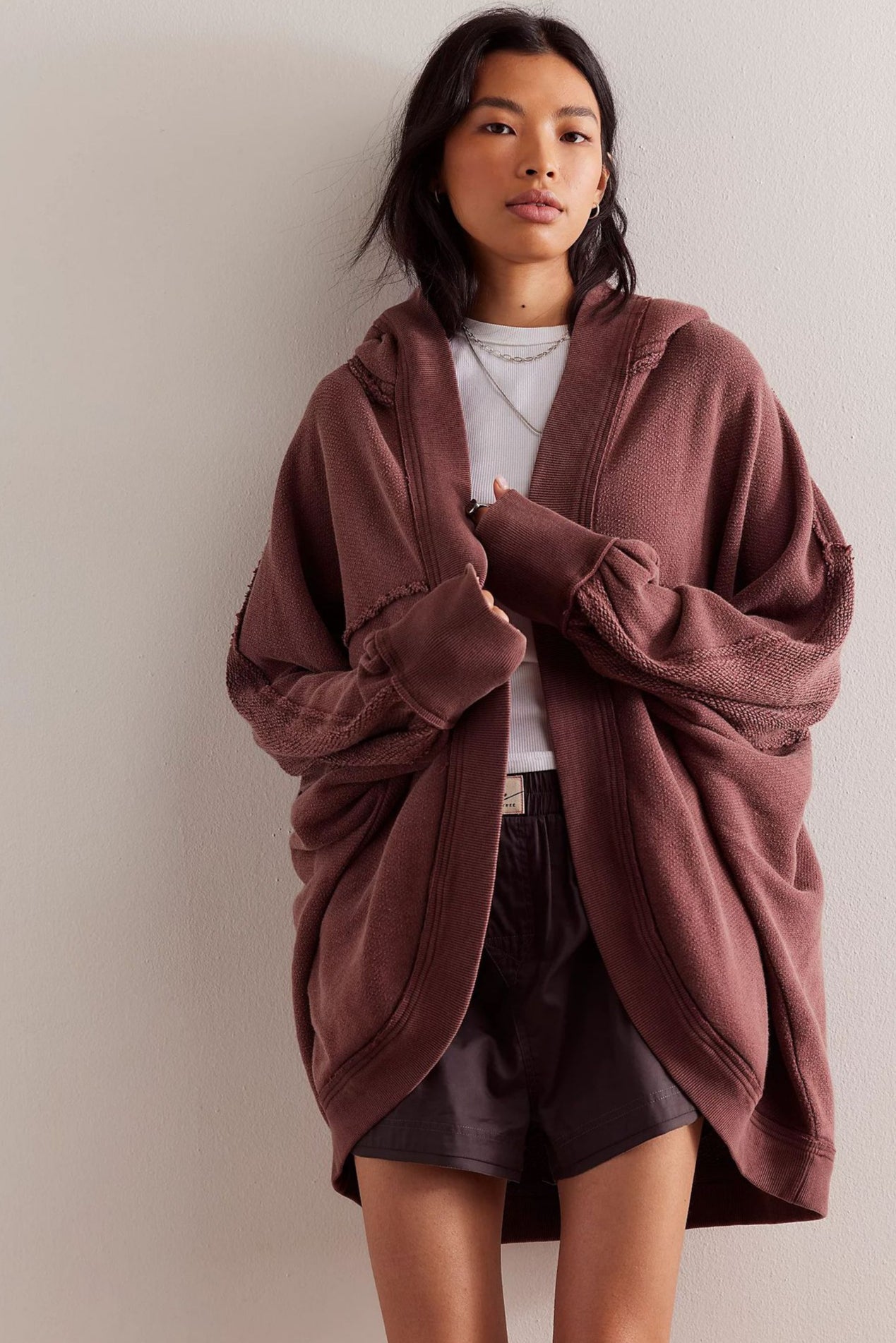 Donna con felpa oversize marrone, t-shirt bianca e pantaloncini neri. Moda casual, abbigliamento comodo, stile urbano.