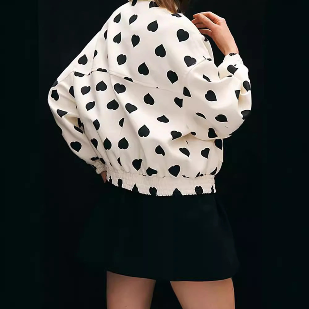 Giacca bianca con stampa a cuori neri, indossata da una donna di spalle, abbinata a una gonna nera. Moda femminile, stile casual chic.