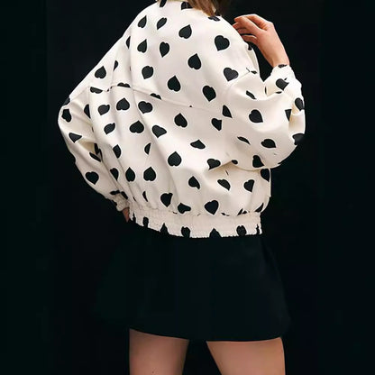 Giacca bianca con stampa a cuori neri, indossata da una donna di spalle, abbinata a una gonna nera. Moda femminile, stile casual chic.