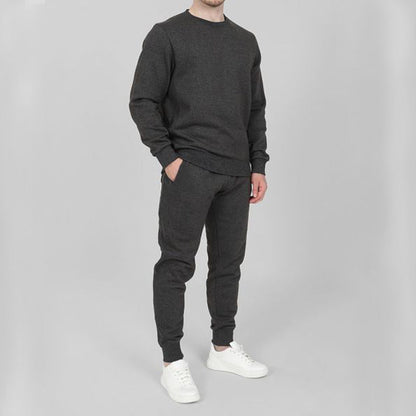 Uomo in tuta sportiva grigia, composta da felpa e pantaloni, con scarpe bianche. Abbigliamento casual e comodo per attività quotidiane.