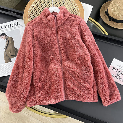 Giacca in pile rosa su tavolo nero, accanto a rivista di moda e cappello di paglia. Abbigliamento invernale, moda femminile, stile casual.
