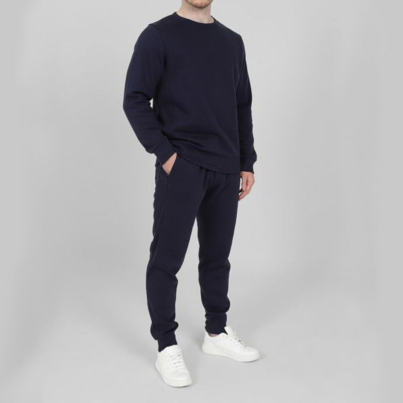 Uomo in tuta sportiva blu scuro, scarpe da ginnastica bianche, sfondo grigio. Abbigliamento casual, moda uomo, comfort quotidiano.
