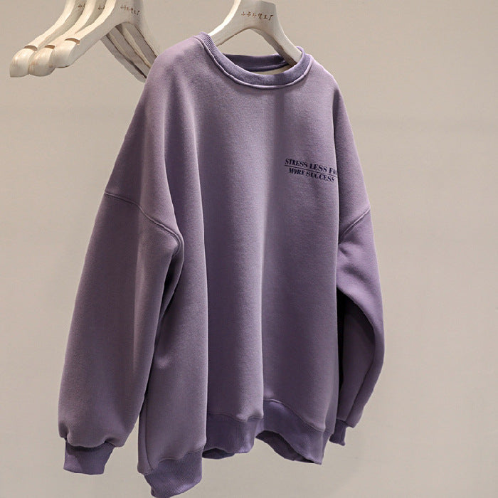 Felpa oversize viola appesa su gruccia, con scritta "Stress Less" sul petto. Moda casual, abbigliamento comodo, tendenza streetwear.